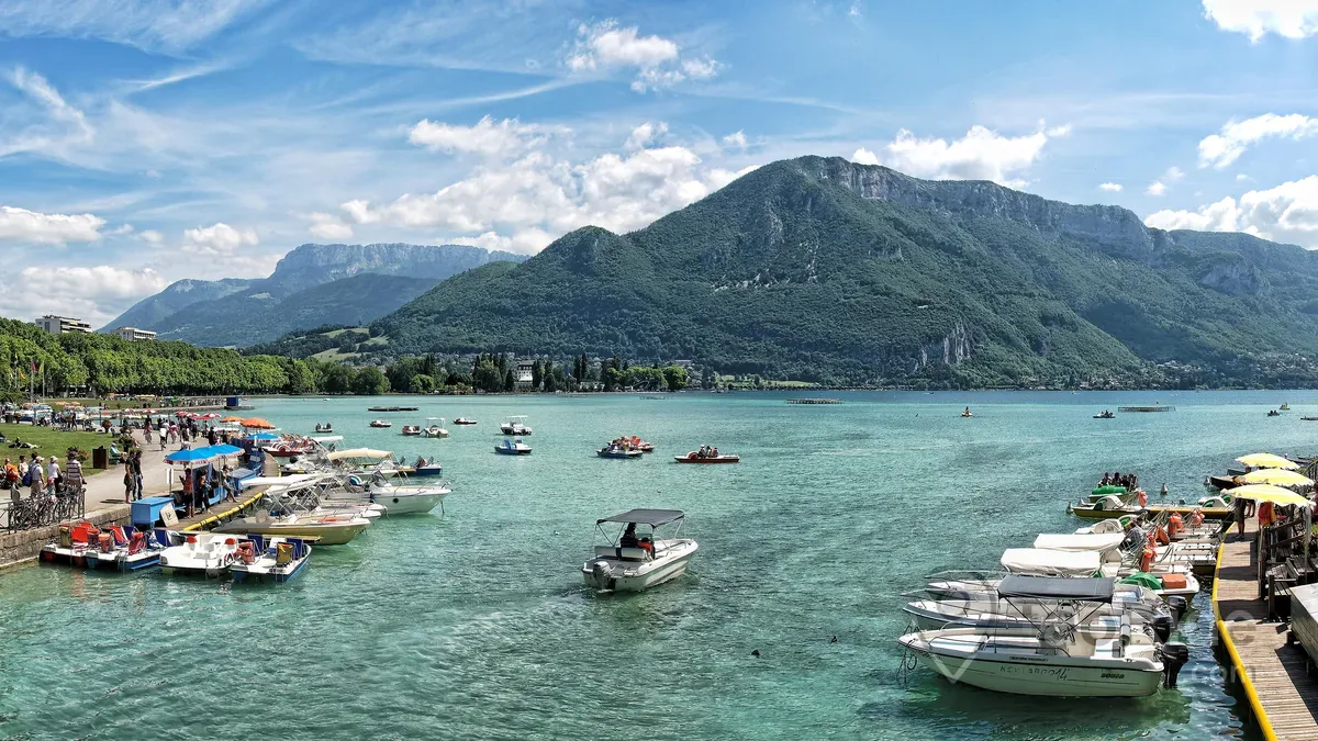 Sunset over Lake Annecy in France with crystal-clear water, the lakeside promenade, sailing boats, and the French Alps creating a breathtaking panoramic landscape.
