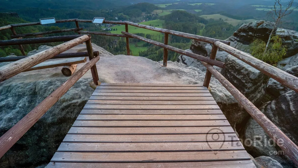 Visitors hiking through Bohemian Switzerland National Park toward Pravčická Gate, surrounded by sandstone cliffs, forest trails, scenic viewpoints, and the picturesque village of Hřensko.